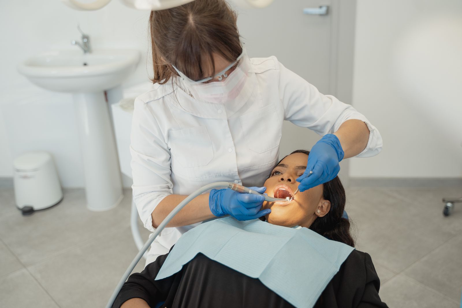 A female dentist wearing a facemask examines a patient's teeth in a dental clinic.